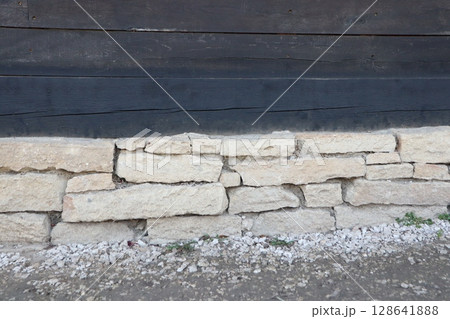 A rustic stone wall base stands proudly against a charming wooden structure nearby A rustic stone wall base stands proudly against a charming wooden structure nearby 128641888