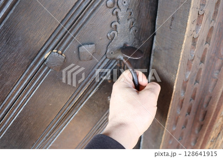 A hand gently reaching out for an intricately designed ornate door handle on a beautiful entrance 128641915
