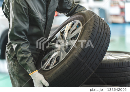 自動車整備工場でタイヤを運ぶ男性メカニック(肉体労働・重労働・重い・腰痛) 自動車整備工場でタイヤを運ぶ男性メカニック(肉体労働・重労働・重い・腰痛) 128642093