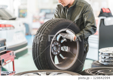 自動車整備工場でタイヤを運ぶ男性メカニック（肉体労働・重労働・重い・腰痛） 128642094