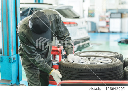 自動車整備工場でタイヤを運ぶ男性メカニック(肉体労働・重労働・重い・腰痛) 自動車整備工場でタイヤを運ぶ男性メカニック(肉体労働・重労働・重い・腰痛) 128642095