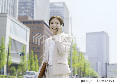 オフィス街でスマホで会話する若いビジネスウーマンのポートレート オフィス街でスマホで会話する若いビジネスウーマンのポートレート 128642454