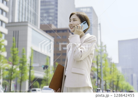 オフィス街でスマホで会話する若いビジネスウーマンのポートレート オフィス街でスマホで会話する若いビジネスウーマンのポートレート 128642455