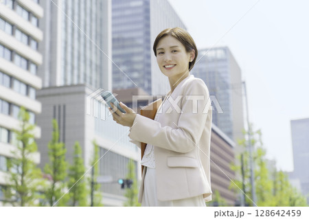 オフィス街でスマホを操作する若いビジネスウーマンのポートレート 128642459