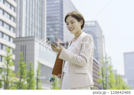 オフィス街でスマホを操作する若いビジネスウーマンのポートレート 128642460