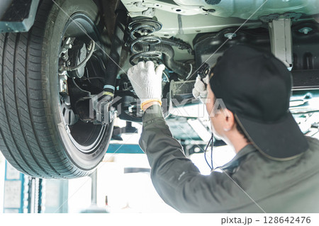 リフトに上がる車両の下で整備・点検・作業をする自動車整備士の男性 リフトに上がる車両の下で整備・点検・作業をする自動車整備士の男性 128642476
