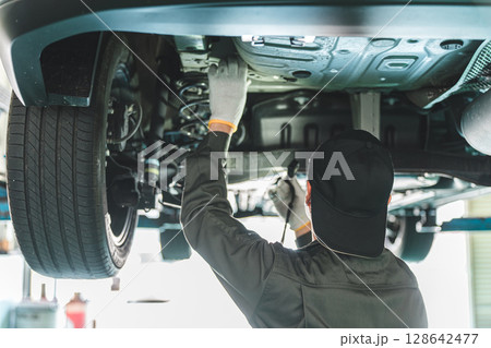 リフトに上がる車両の下で整備・点検・作業をする自動車整備士の男性 リフトに上がる車両の下で整備・点検・作業をする自動車整備士の男性 128642477