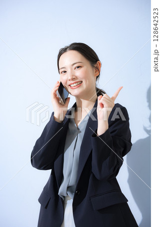 電話をかける通話するスーツを着た若い女性のビジネスシーン　背景水色	 128642523