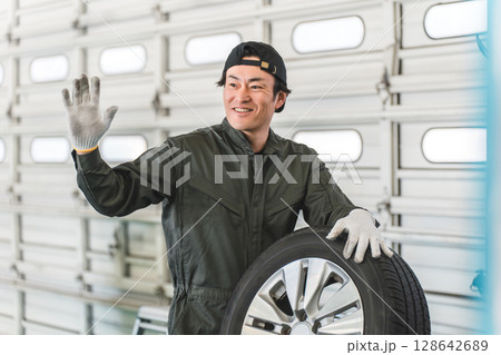 タイヤを持って挨拶する自動車整備士・メカニックの中年アジア人男性 128642689