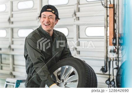 タイヤを持って挨拶する自動車整備士・メカニックの中年アジア人男性 タイヤを持って挨拶する自動車整備士・メカニックの中年アジア人男性 128642690