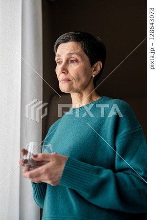 Exhausted woman with water medicine by window in stillness alone. Emotional tress, quiet reflection 128643078