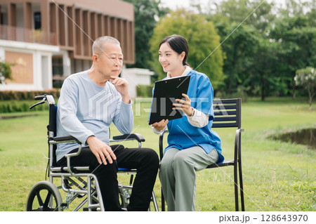 Asian careful caregiver or nurse and the happy patient in a wheelchair are walking in the garden. to help and encourage and rest your mind with green nature. Use a stethoscope to listen Asian careful caregiver or nurse and the happy patient in a wheelchair are walking in the garden. to help and encourage and rest your mind with green nature. Use a stethoscope to listen 128643970