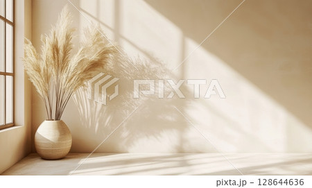 A serene interior scene featuring a light-colored wall, a decorative vase with dried flowers, and soft shadows created by natural sunlight streaming through a window. 128644636