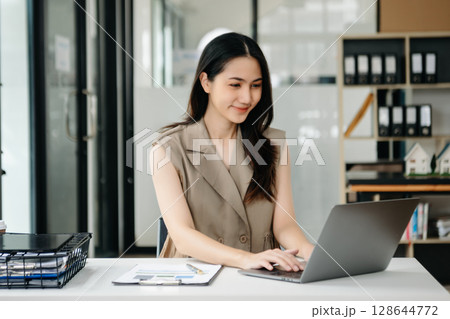 Young beautiful woman using laptop and tablet while sitting at her working place. Concentrated at work. 128644772