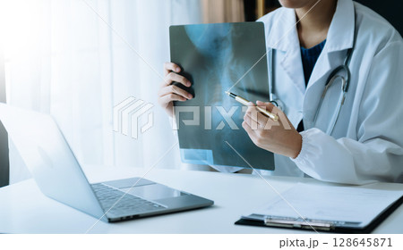 woman doctor showing x-ray lap sheet and explain the details to patient via video call system at the hospital. 128645871