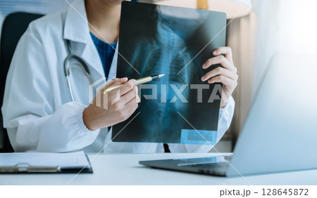 woman doctor showing x-ray lap sheet and explain the details to patient via video call system at the hospital. 128645872