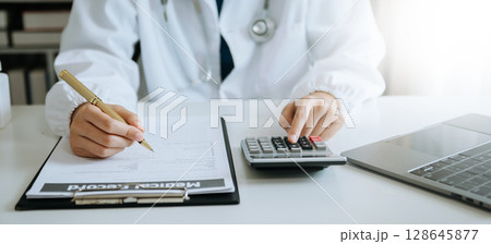 Healthcare costs and fees concept.Hand of smart doctor used a calculator and smartphone, tablet for medical costs at hospital 128645877