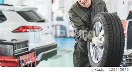 自動車整備工場でタイヤを運ぶ男性メカニック(肉体労働・重労働・重い・腰痛) 自動車整備工場でタイヤを運ぶ男性メカニック(肉体労働・重労働・重い・腰痛) 128645976