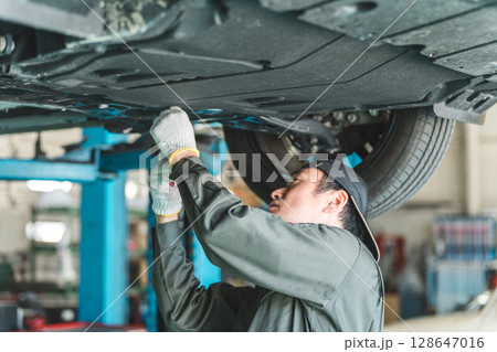 リフトに上がる車両の下で整備・点検・作業をする自動車整備士の男性 リフトに上がる車両の下で整備・点検・作業をする自動車整備士の男性 128647016