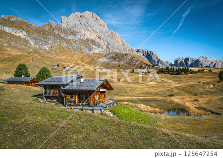 Alpine lake and wooden lodges on the slope, Dolomites, Italy 128647254