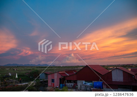 Dramatic sky with vivid sunset colors over tin houses and distant landscape that shows the candid scene of daily life in the rural countryside of Kampot, Cambodia 128647636