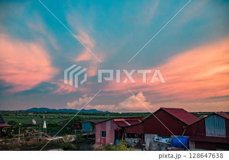 Serene summer sunset pink clouds over tin houses and expansive fields in the rural countryside of Kampot Cambodia showing candid daily life Serene summer sunset pink clouds over tin houses and expansive fields in the rural countryside of Kampot Cambodia showing candid daily life 128647638