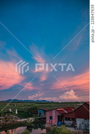 Tranquil summer sunset scene with a colorful sky and distant fields stretching beyond rooftops of tin houses in the rural countryside of Kampot, Cambodia Tranquil summer sunset scene with a colorful sky and distant fields stretching beyond rooftops of tin houses in the rural countryside of Kampot, Cambodia 128647639