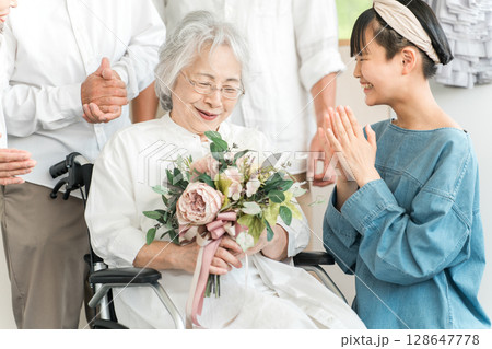 車椅子に乗るおばあちゃんに花束をプレゼントする笑顔の孫娘 128647778
