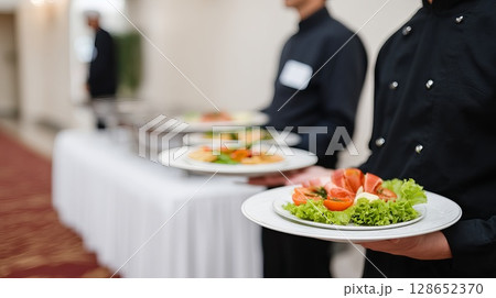 Professional Waitstaff Serving Plates of Fresh Salad and Appetizer in Elegant Dining Setting 128652370