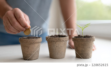 Person Investing in Growth with Coins and Small Plants in Pots on a Table in Bright Setting Person Investing in Growth with Coins and Small Plants in Pots on a Table in Bright Setting 128652615
