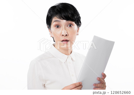 書類を見て目を見開き驚いた表情の中年女性 128652660