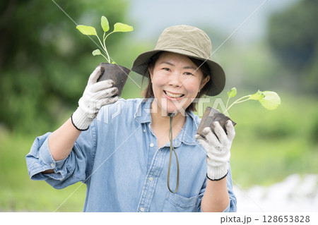 畑でナスの苗植え作業する女性　農家や農業で働くする人のイメージ　カメラ目線	 128653828