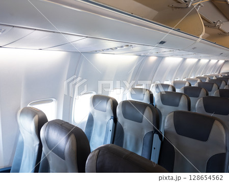 Empty airplane cabin with row of gray seats and overhead bins 128654562