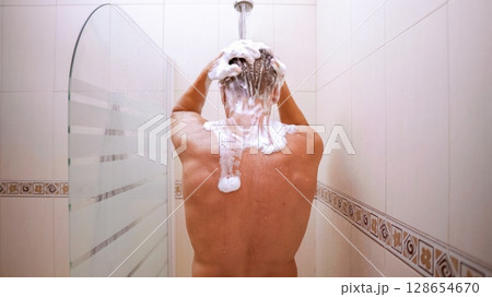 Man washing hair with shampoo in shower, back view Man washing hair with shampoo in shower, back view 128654670