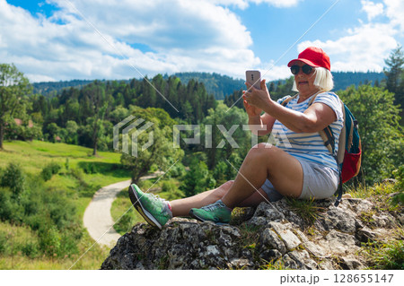 Smiling senior woman taking a selfie while hiking in the mountains 128655147