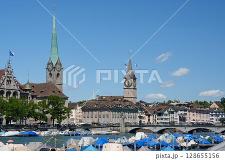 Zurich, clock towers and a promenade with boats. Switzerland with the legendary clock towers - the Fraumunster and St. Peter churches. Zurich, clock towers and a promenade with boats. Switzerland with the legendary clock towers - the Fraumunster and St. Peter churches. 128655156