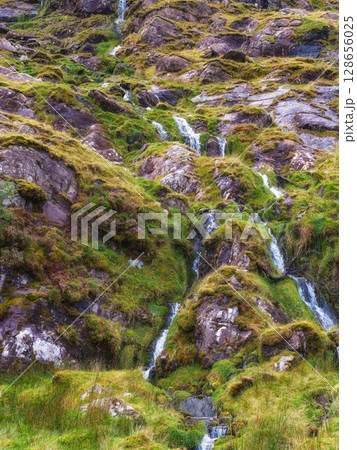 Cascading waterfalls flow down mossy rocks along carrauntoohil mountain walkway in county kerry, republic of ireland. 128656025