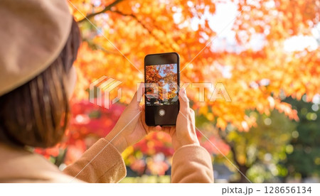 《AI画像》秋の紅葉をスマホで撮影する若い女性 128656134