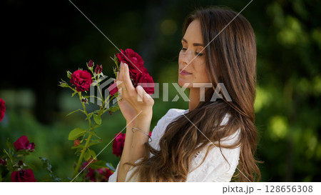 Peaceful woman holding red rose in blooming garden 128656308