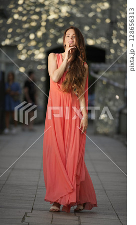 Confident woman posing in coral dress with sparkling bokeh in city 128656313