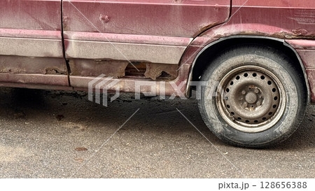 An old car that is showing significant rust and wear, complete with a visibly damaged side panel, indicating neglect An old car that is showing significant rust and wear, complete with a visibly damaged side panel, indicating neglect 128656388