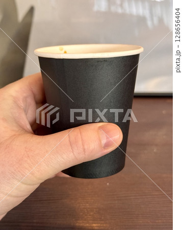 Unknown hand holding brown disposable paper cup with coffee from first face. Close-up 128656404