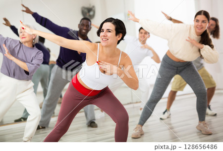 Cheerful young lady learning new modern dance in group dance lesson Cheerful young lady learning new modern dance in group dance lesson 128656486