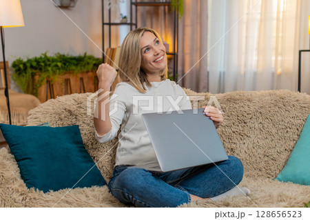 Adult woman celebrating at home after completing work on laptop, raising arm with joy satisfaction Adult woman celebrating at home after completing work on laptop, raising arm with joy satisfaction 128656523