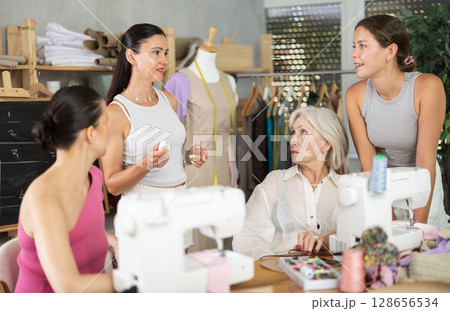 Experienced seamstress giving sewing lesson to group of female students Experienced seamstress giving sewing lesson to group of female students 128656534