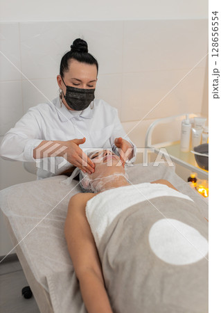 Woman receiving facial gauze wrap for carboxytherapy in cosmetology skin covered with serum moisture 128656554
