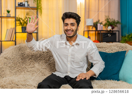 Indian young man smiling, waving hand at camera, greeting warmly, friendly communication, video call Indian young man smiling, waving hand at camera, greeting warmly, friendly communication, video call 128656618