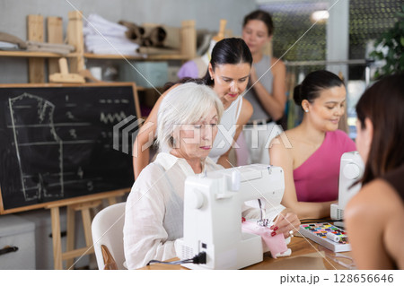 Elderly female teacher shows group how to sew 128656646