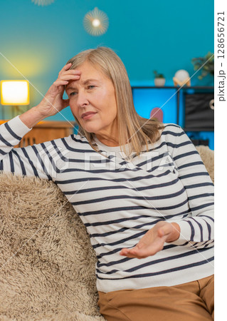 Mature woman placing hand on forehead on sofa showing frustration helplessness after bad day at home Mature woman placing hand on forehead on sofa showing frustration helplessness after bad day at home 128656721