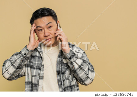 Disinterested tired Asian man having annoyed boring talk on smartphone online conversation quarrel 128656743